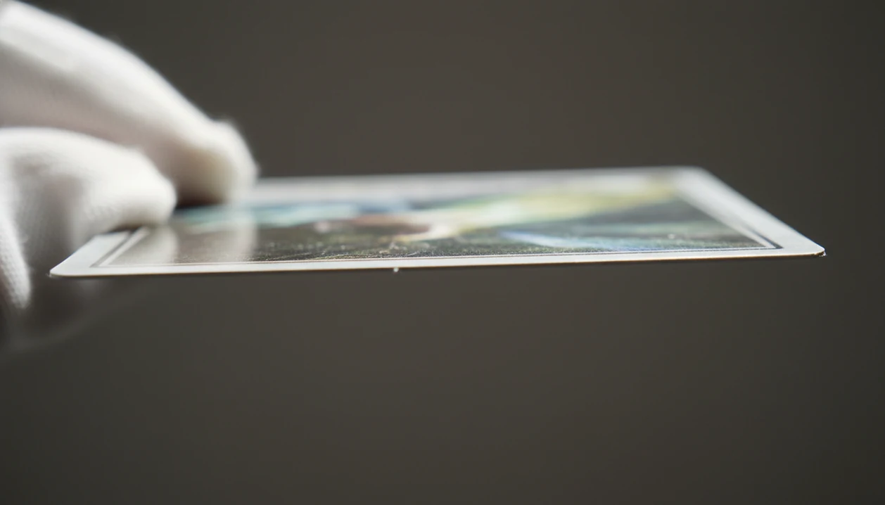 A macro view shows a gloved hand inspecting a trading card corner for whitening, scuffs, and surface wear.